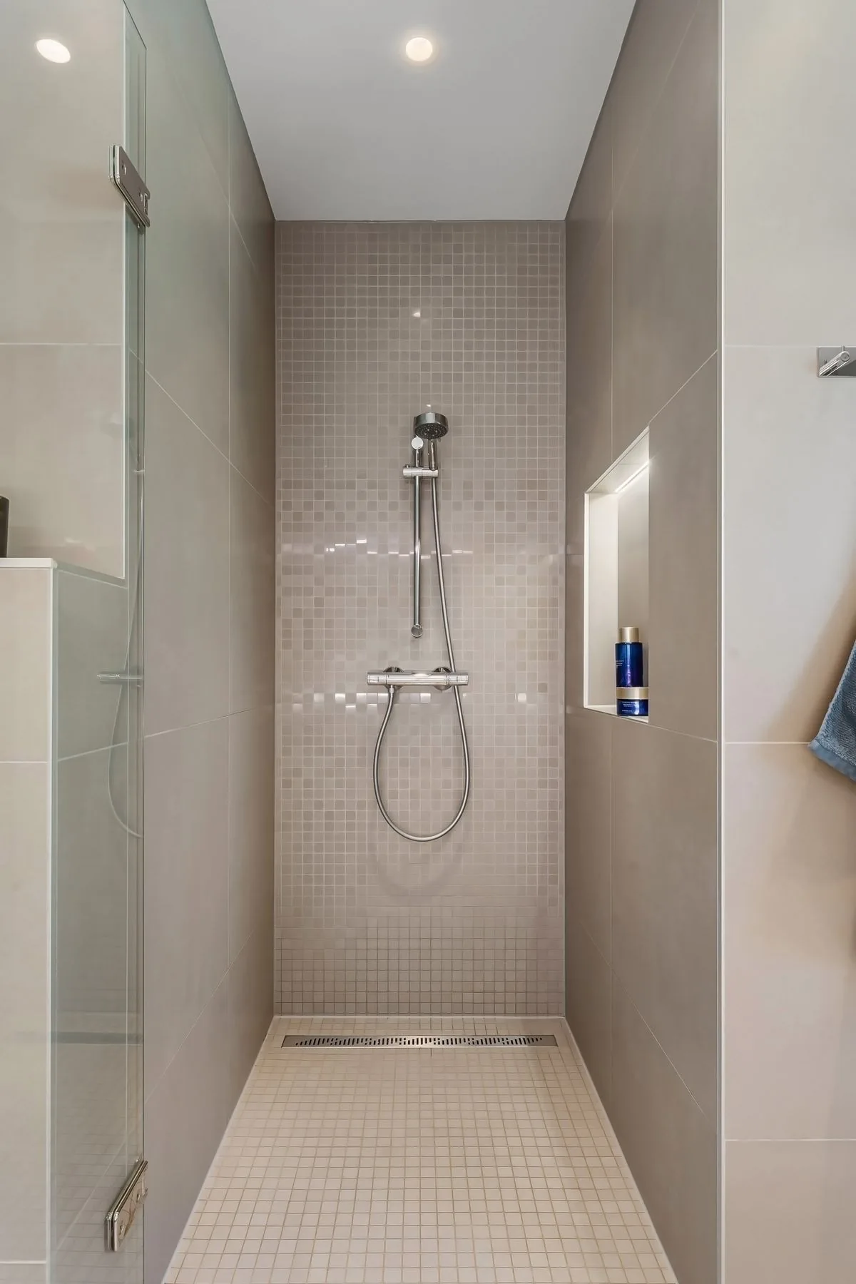 Bodengleiche Dusche mit Glastrennwand, beigen Fliesen und beleuchteter Ablagenische