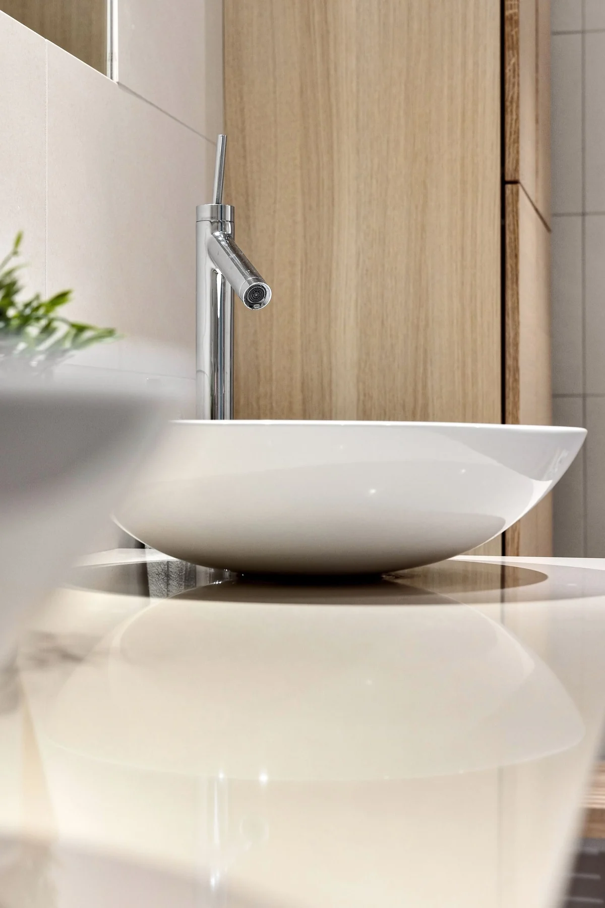 Weißes Aufsatzwaschbecken mit Chromarmatur vor einer hellen Holzoberfläche